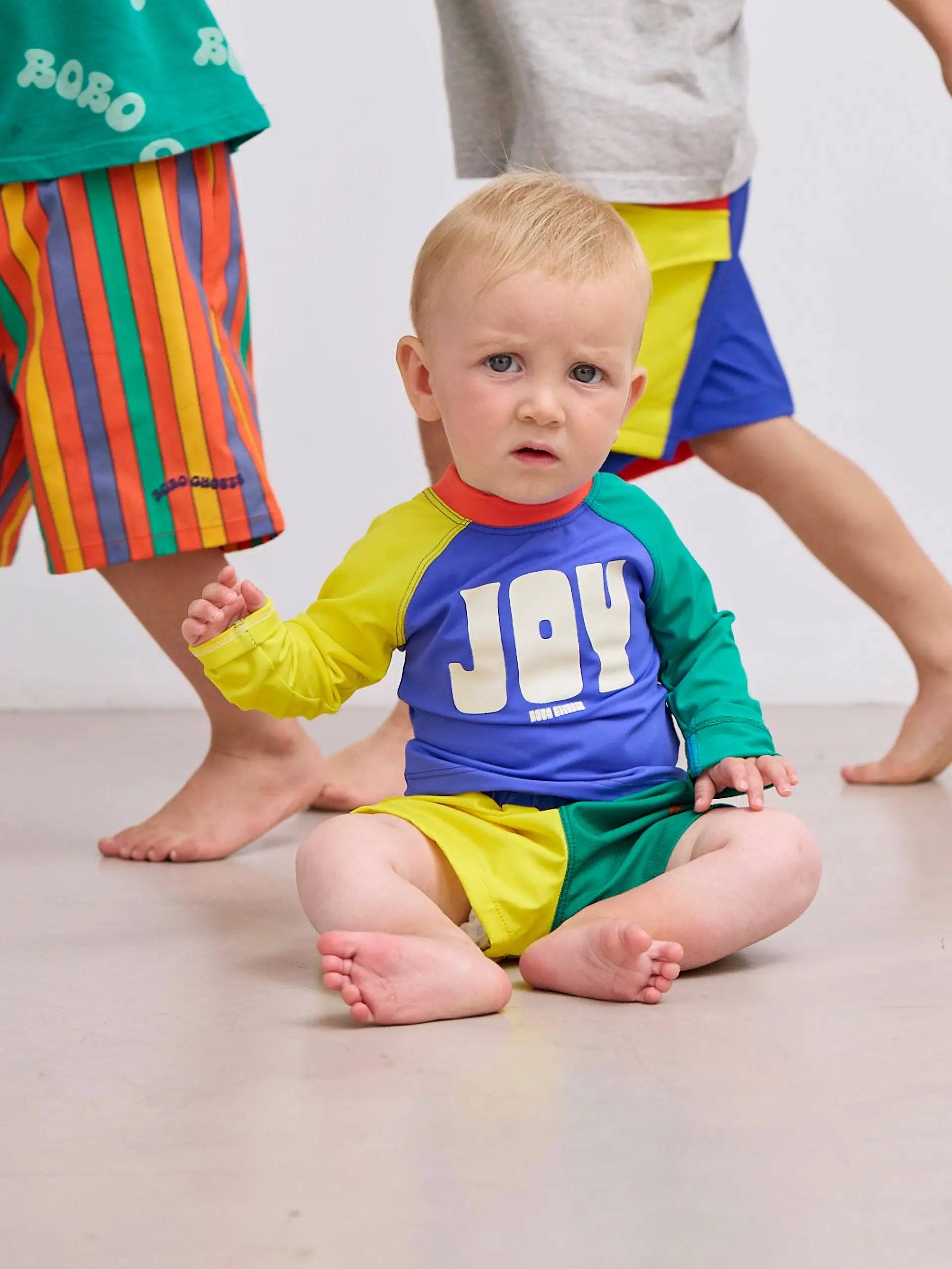Baby trägt farbblockierte Baby Color Block Swim Trunks in Gelb, Grün und Blau aus der SS25 Kollektion von Bobo Choses. Perfekt für 0–24 Monate.
