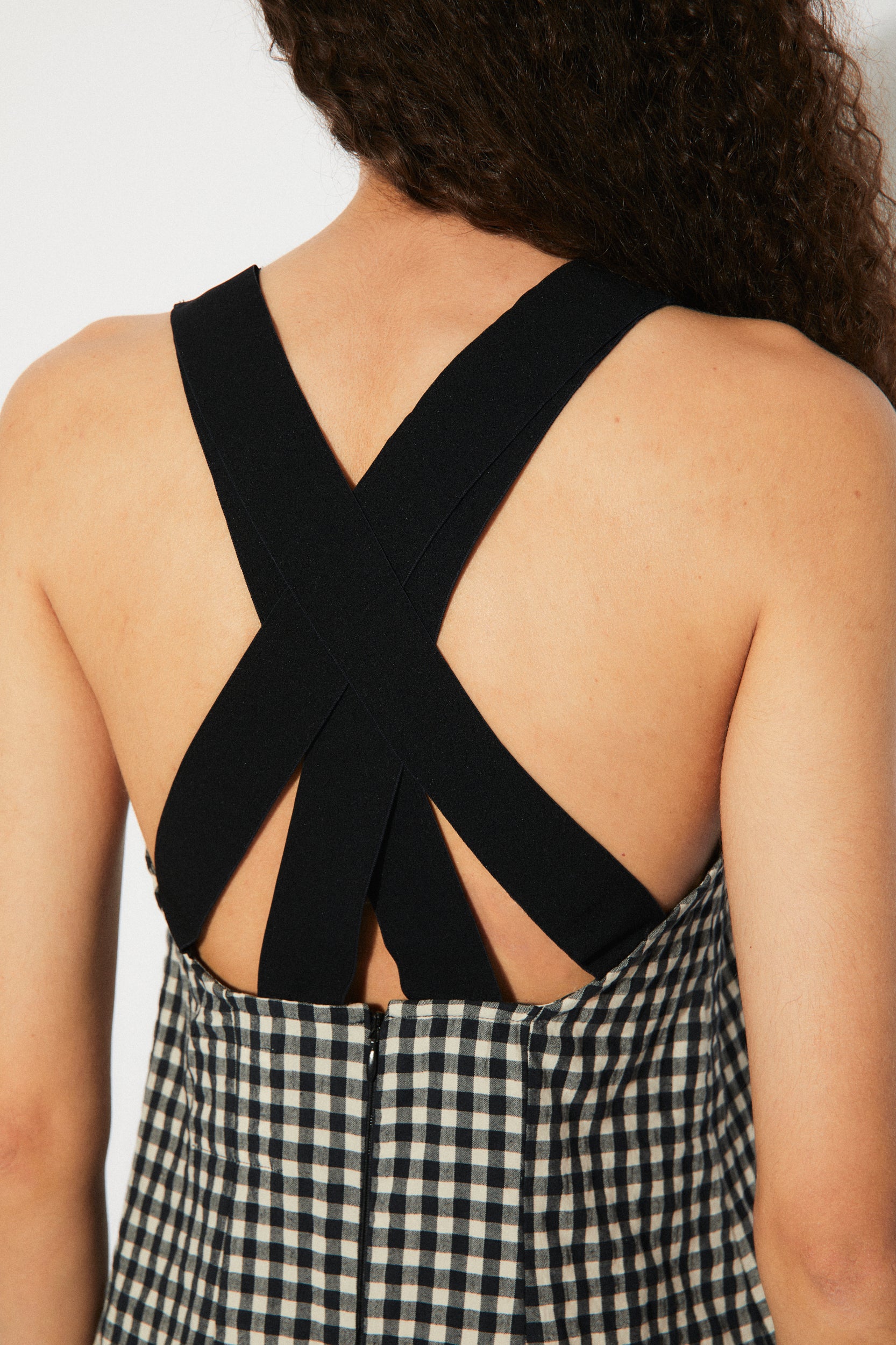 Close-up of the Oyster Dress Black Gingham's crisscross back straps and zipper detail. A sophisticated and trendy choice for women’s fashion.