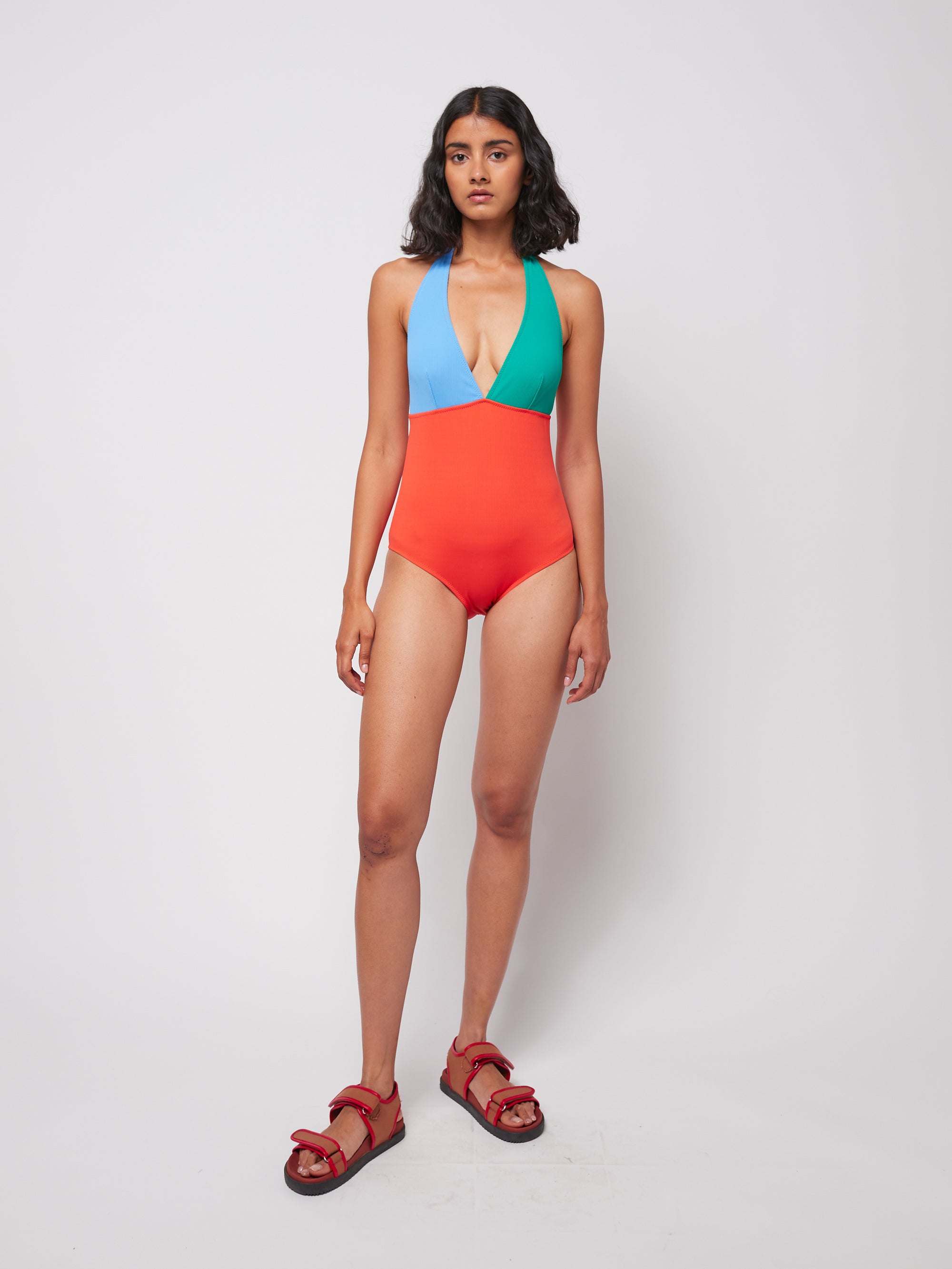 Model wearing Color Block V-Neck Swimsuit with blue, green, and red panels, made in Spain from polyamide and elastane.