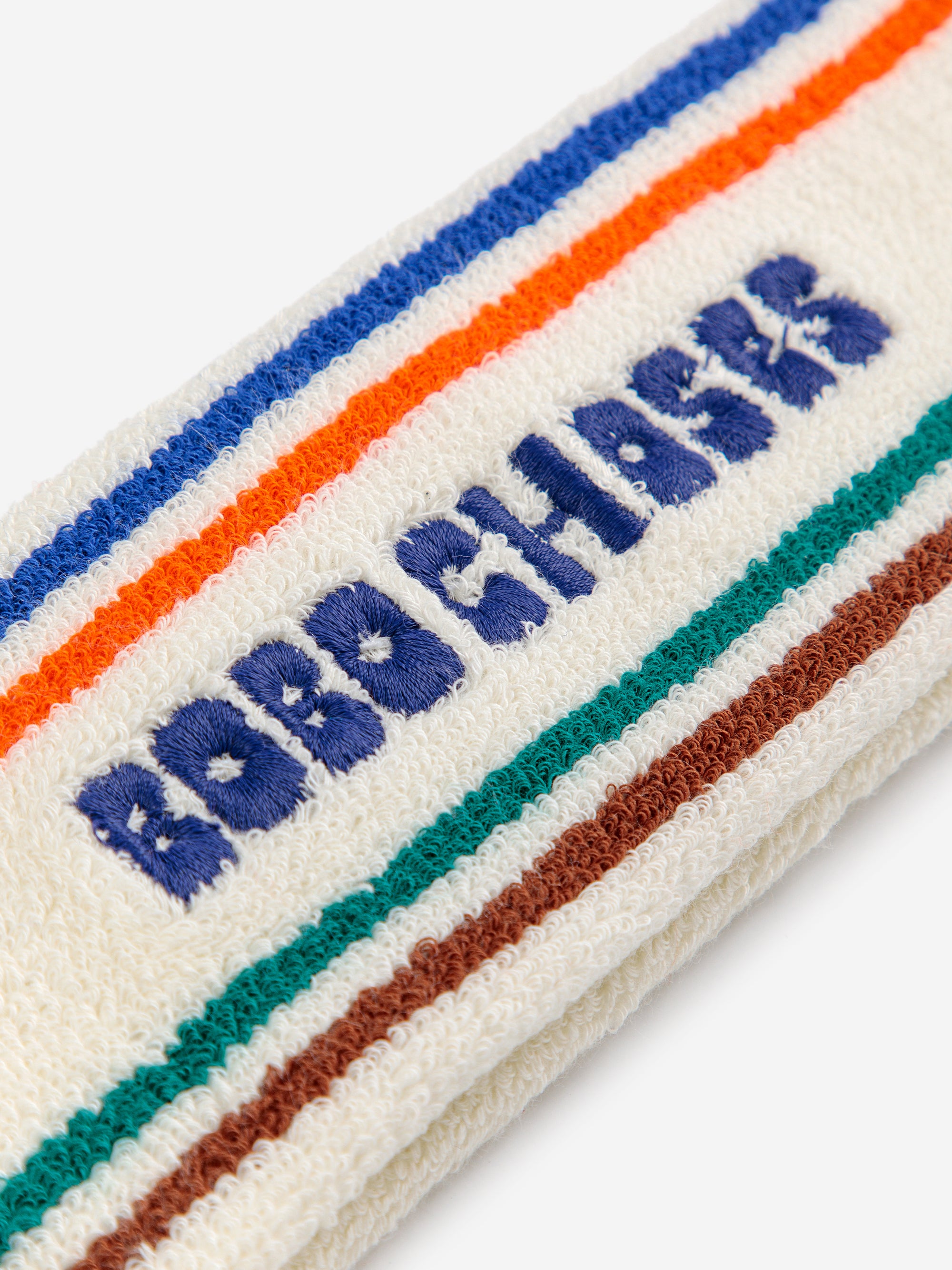 Close-up of Bobo Choses Stripes Terry Headband. Showcasing textured terry fabric with detailed embroidered logo and colorful stripe accents.