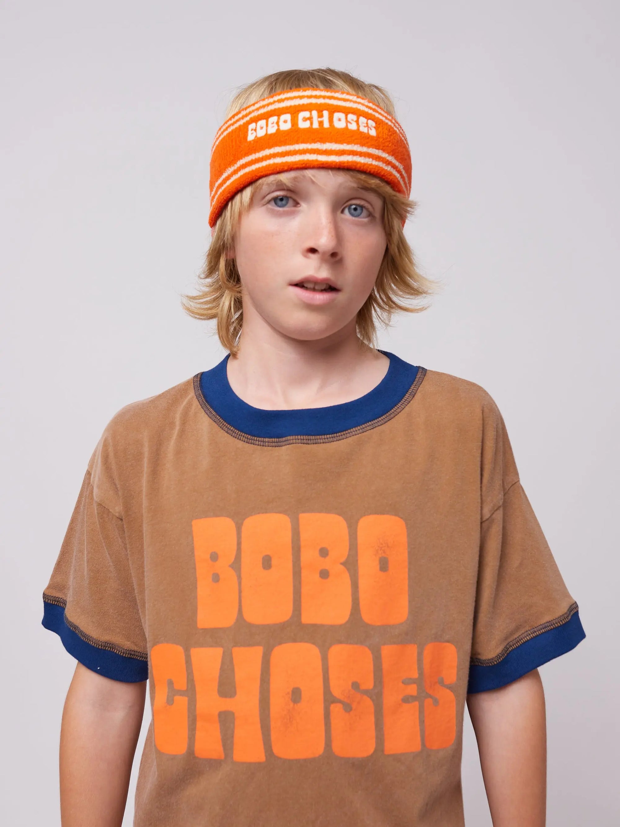 Child wearing Bobo Choses Orange Terry Towel Headband, a soft and absorbent accessory made in Spain, paired with a matching brown and orange t-shirt.