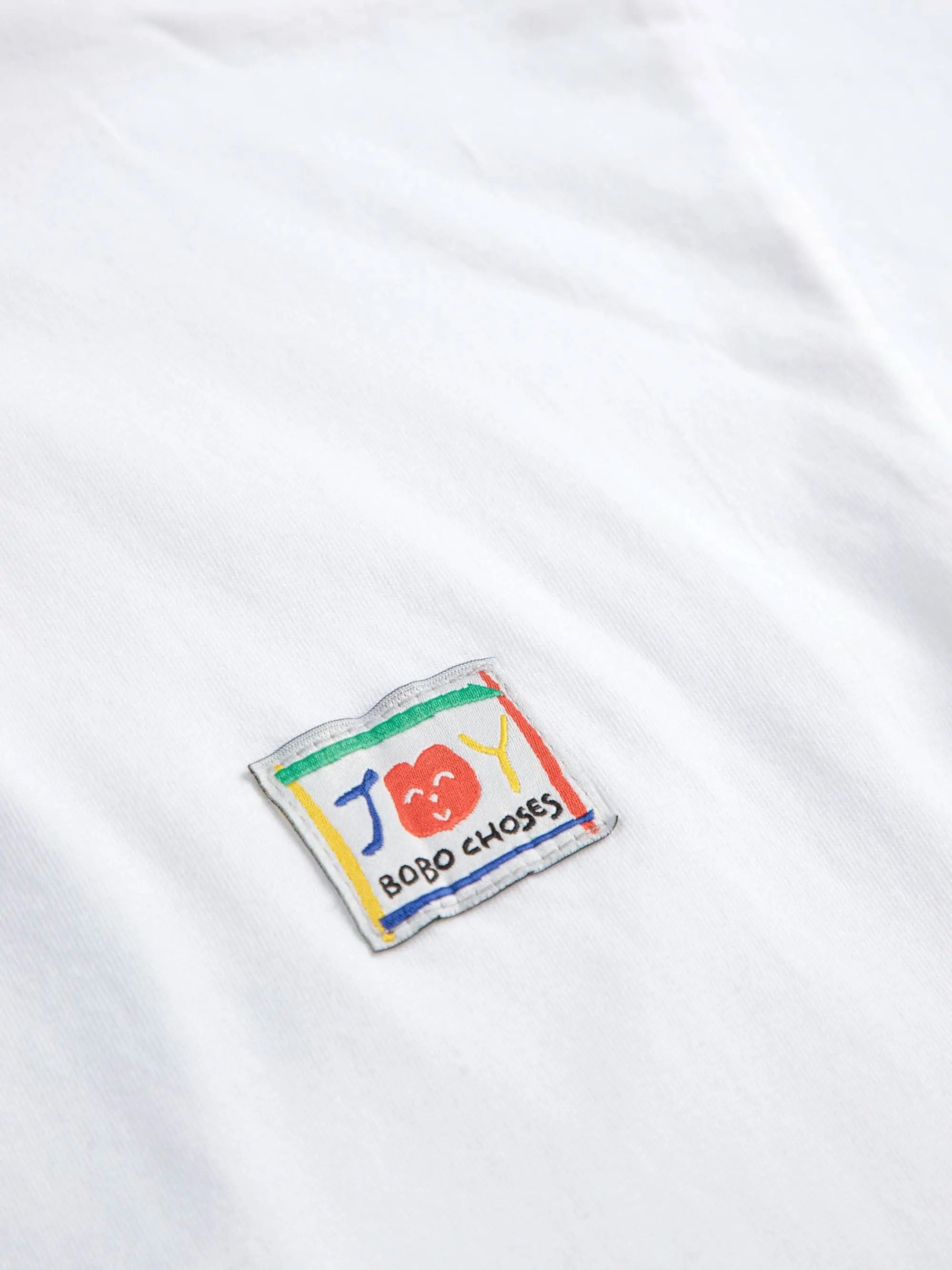 Detailansicht des Hello Joy Logos auf der Brust mit buntem Design und Bobo Choses Schriftzug. Hochwertiger Aufnäher für Kinderbekleidung.