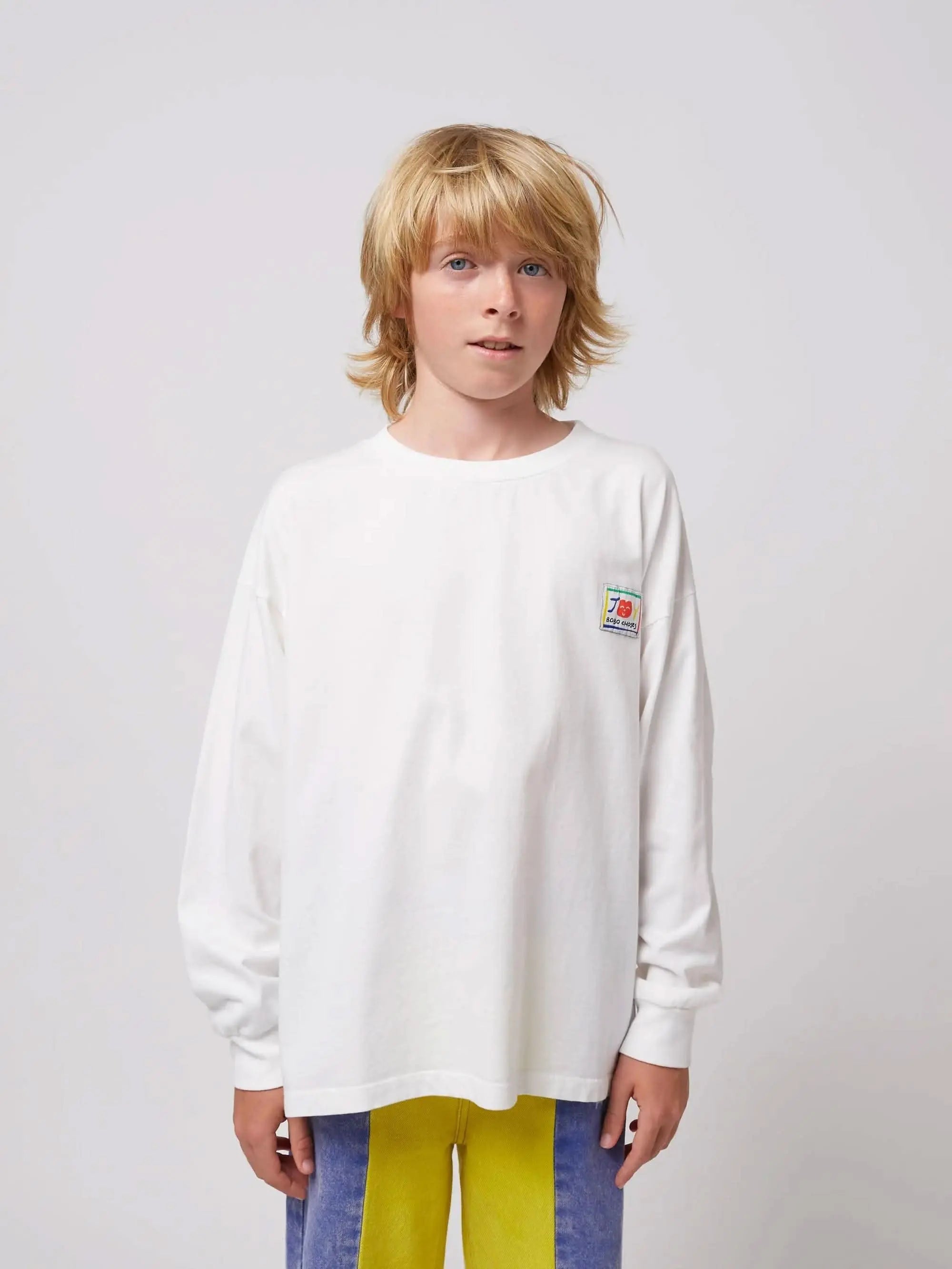 Weißes Hello Joy T-Shirt mit kleinem bunten Logo auf der Brust, locker geschnitten für Jungen und Mädchen. Teil der neuen SS25 Kollektion.