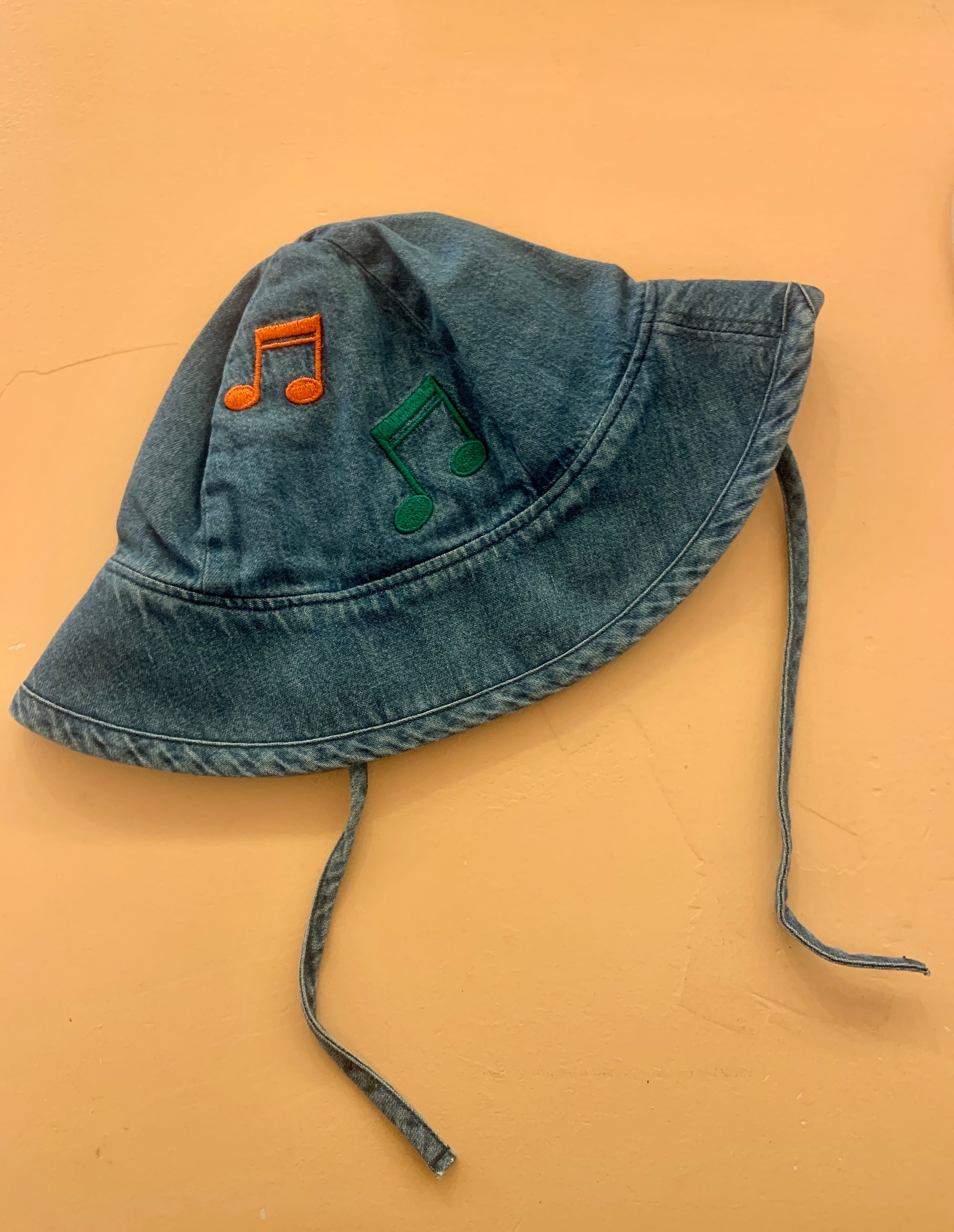 Note EMB Sun Hat in denim blue with embroidered orange and green musical notes. Features a wide brim and adjustable chin straps for a secure fit.