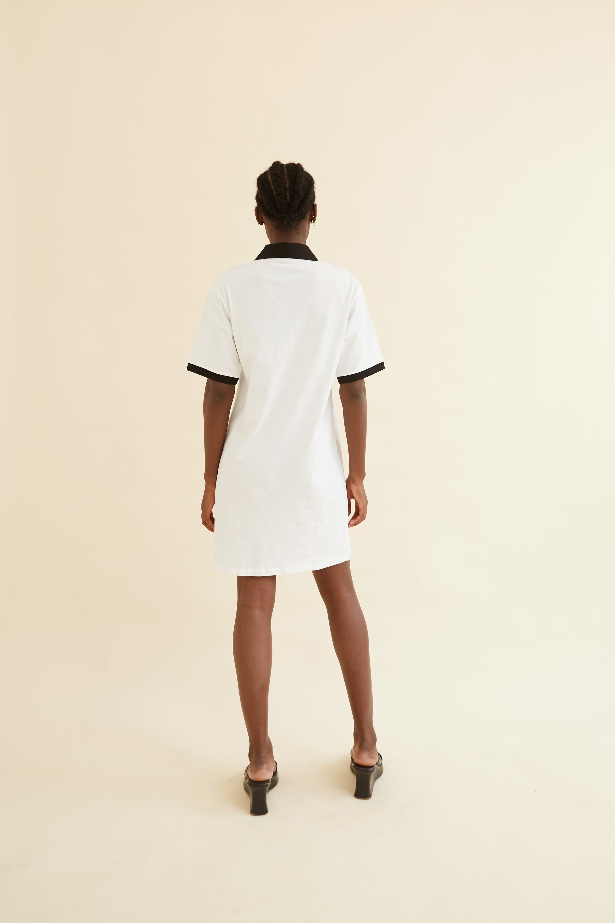 Back view of the Josephine Polo Dress, showcasing its minimalistic design with a black collar and sleeve trim on a white fabric for a chic finish.