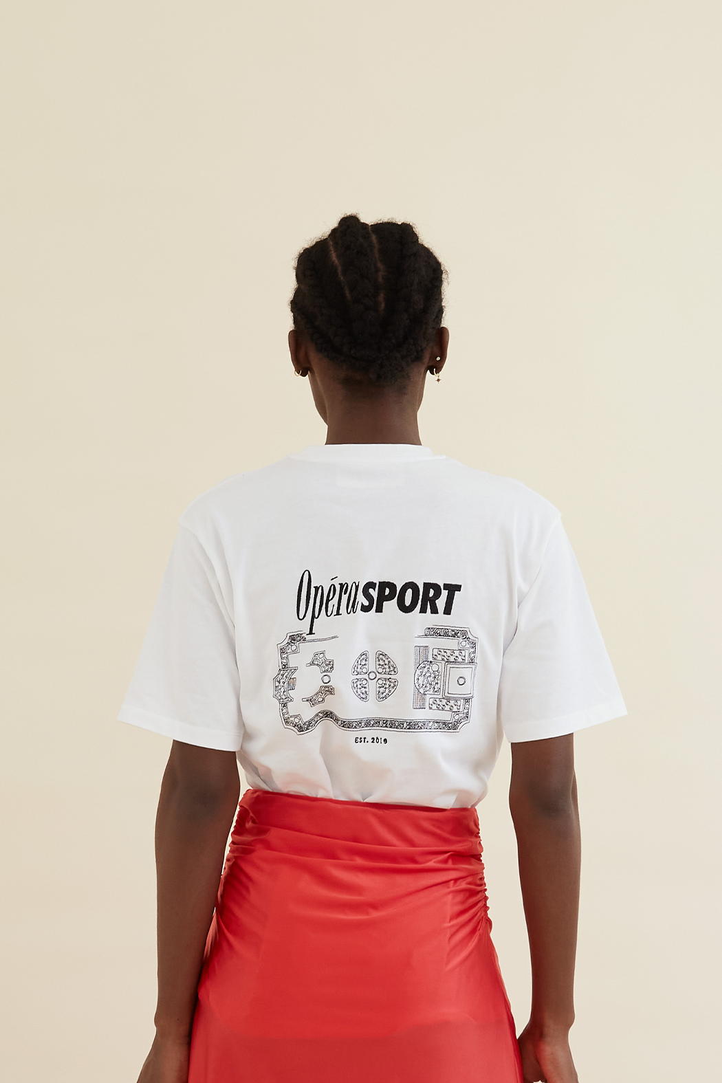 Back view of the Organic Cotton Unisex T-Shirt White, showcasing a bold black OpéraSPORT graphic print. Styled with a red ruched skirt.