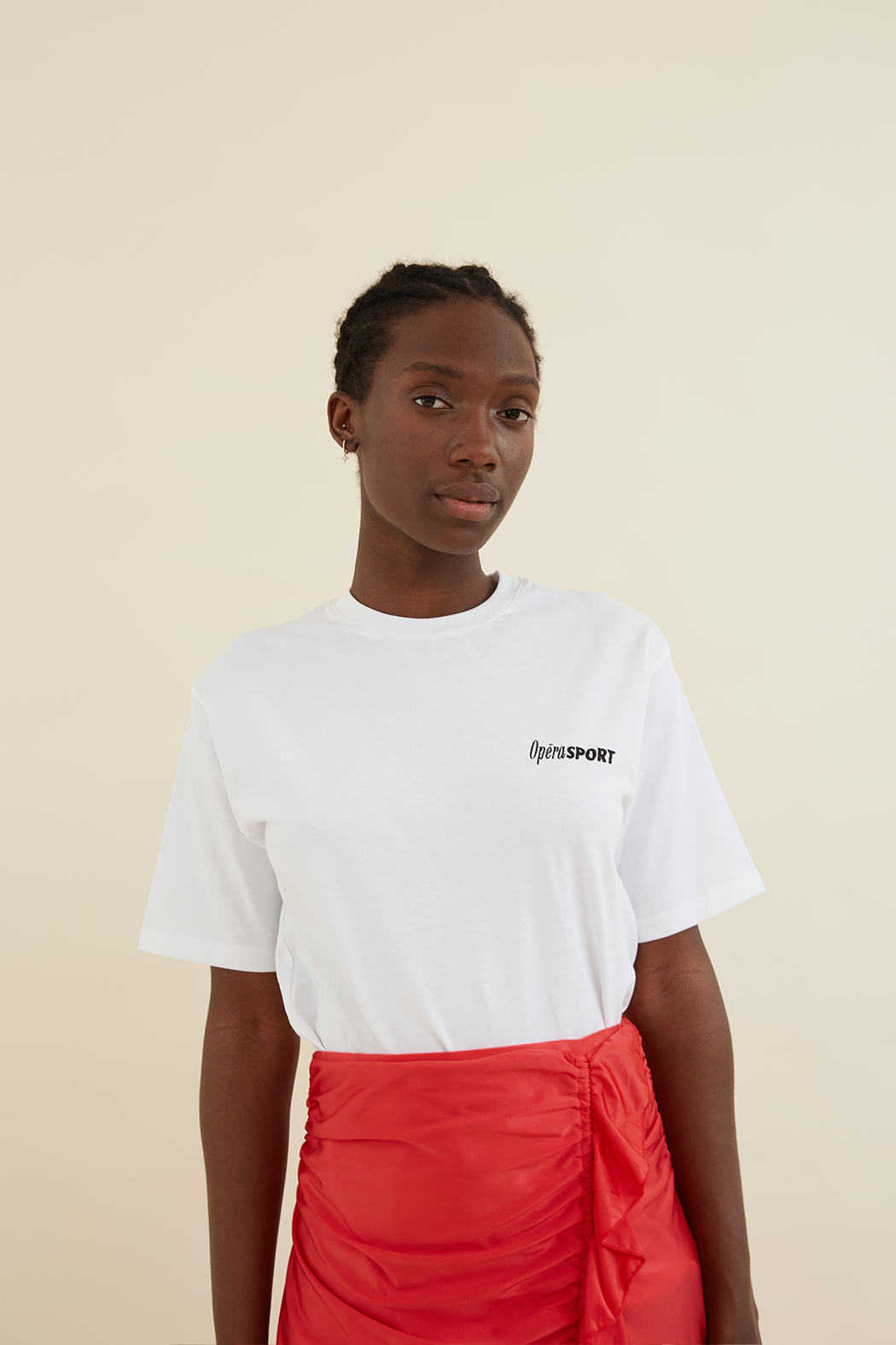 Organic Cotton Unisex T-Shirt White with a relaxed fit, round neckline, and small OpéraSPORT logo on the front. Styled with a red ruched skirt.